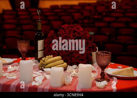 Romantico tavolo in teatro: Rose rosse, vino, frutta, candele, scena drammatica, amore, San Valentino, atmosfera interna di colore rosso scuro Foto Stock