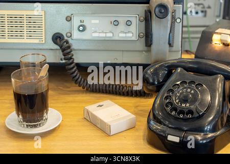 Telefono rotativo vintage, dispositivo di comunicazione rétro, bevande e sigarette su un tavolo di legno Foto Stock