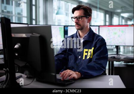 L'agente dell'FBI senior con più monitor lavora diligentemente in ufficio. Foto Stock