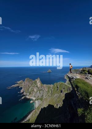 Un escursionista gode di splendide vedute panoramiche dal monte Matind, circondato da scogliere spettacolari e dalle acque azzurre del mare norvegese vicino a Bleik sull'isola di Andoya. Foto Stock