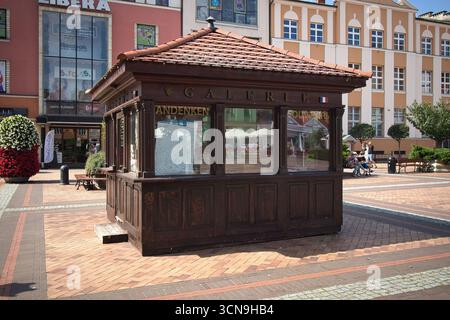 Una piccola struttura in legno con un cartello che dice Galleria. La struttura è circondata da un passaggio pedonale in mattoni e ha alcune piante in vaso nelle vicinanze. La scena A. Foto Stock