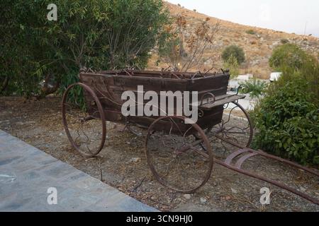 Un carro di legno con ruote in metallo arrugginito si trova su un sentiero accanto a una collina rocciosa e asciutta a Creta. Foto Stock