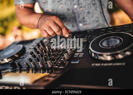 Milano, italia 20 settembre 2025: dj che regola a mano fader e manopole su un moderno controller mixer audio, creando un'atmosfera vibrante a un livello all'aperto Foto Stock