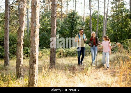 Una famiglia passeggia attraverso una foresta lussureggiante, circondata da alberi alti e vegetazione, godendosi del tempo di qualità insieme in una giornata di sole. Foto Stock