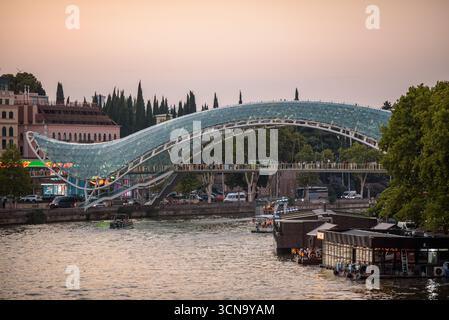 Vista del tramonto del ponte della Pace, del ponte pedonale in acciaio e vetro sul fiume Kura Mtkvari nel centro di Tbilisi, capitale della Georgia al 20 agosto Foto Stock