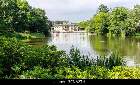 Varsavia, Polonia,13.07.21. Il Palazzo sull'isola (in polacco: Palac Na Wyspie) nel Parco reale delle terme di Varsavia, paesaggio con vegetazione lussureggiante e gondola rossa Foto Stock
