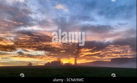 Un'alba unica nella campagna svizzera con spettacolari formazioni nuvolose e raggi visibili di luce del sole che illuminano il paesaggio Foto Stock