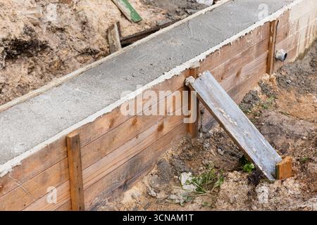 Una parete in cassaforma di legno confina con una lastra di cemento appena versata in un cantiere attivo. Una pedana resistente agli agenti atmosferici funge da rampa temporanea contro lo sporco Foto Stock