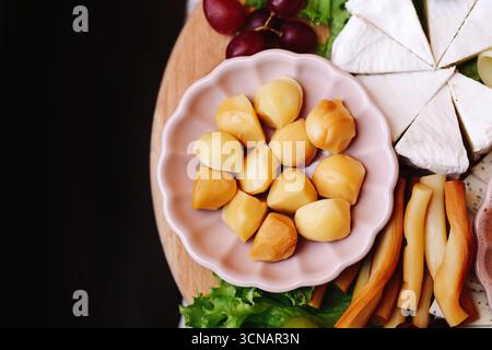 Pezzi di formaggio affumicato sul piatto. Tradizionale spuntino a base di latte con formaggi assortiti. Antipasto rustico al tavolo della festa. Viene servito un prodotto gourmet fresco. Foto Stock