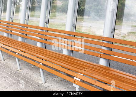 Panchine in legno alla fermata dell'autobus. Lunga fila di posti a sedere in un rifugio moderno. Progettazione dei trasporti pubblici e delle infrastrutture urbane. Foto Stock