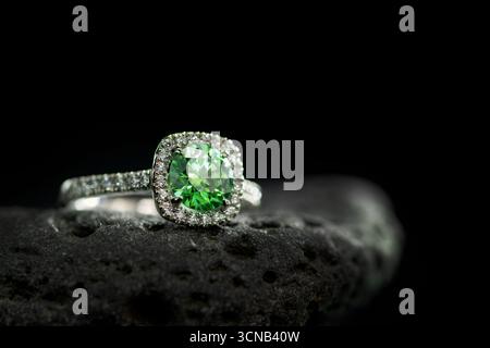 Un anello verde di pietre preziose si trova su una roccia. L'anello è fatto d'oro e ha un diamante al centro. La pietra è circondata da una banda di diamanti, donando Foto Stock