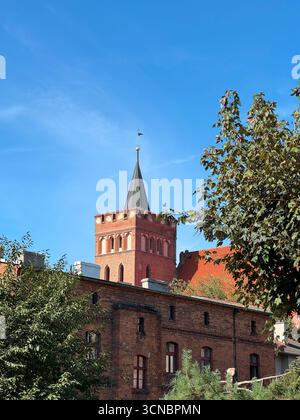 Storica chiesa cattolica costruita nel XIV secolo con un'alta torre in mattoni e un ripido tetto rosso, fotografata in una giornata di sole con un cielo azzurro Foto Stock