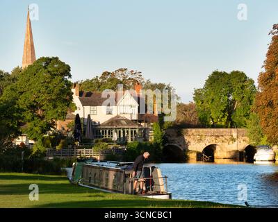 Casa galleggiante ormeggiata sul Tamigi ad Abingdon. Una bella vista del Tamigi ad Abingdon, in tarda mattinata d'estate. Siamo sulla riva sud del fiume, guardando da un'altra parte del ponte medievale di Abingdon. Ancora più antica è la guglia della chiesa anglosassone di Sant'Elena. Foto Stock