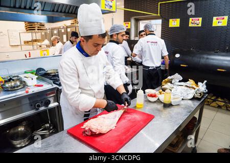BAKU, AZERBAIGIAN-24 MAY2019 : lo chef prepara anche piatti con gambo di agnello. Il processo di cottura dello chef maschio dello stinco di agnello in una cucina professionale. Cucinare Foto Stock