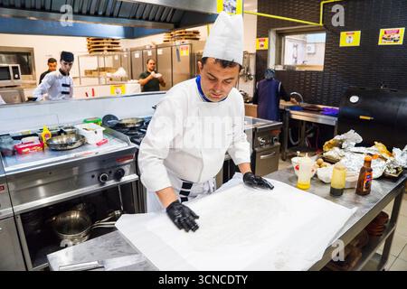 BAKU, AZERBAIGIAN-24 MAY2019 : lo chef prepara anche piatti con gambo di agnello. Il processo di cottura dello chef maschio dello stinco di agnello in una cucina professionale. Cucinare Foto Stock