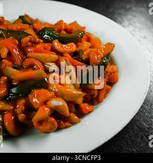 Pollo fritto in padella dolce e acida con verdure, servito con una salsa piccante e guarnito con ingredienti freschi Foto Stock