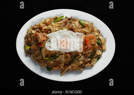 Deliziosi tagliatelle fritte con gamberetti, verdure e un uovo fritto, serviti su un piatto per un gustoso pasto di ispirazione asiatica Foto Stock