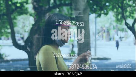 Visualizzazione dei dati numerici della griglia sullo smartphone su un percorso alberato che indossa la parte superiore della senape e la maschera sotto il mento Foto Stock