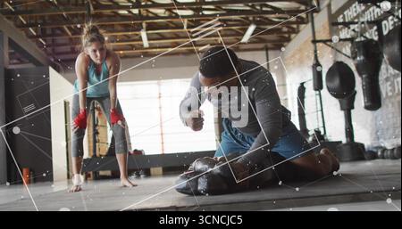 Pugni un afroamericano inginocchiato che fa strike nella palestra di pugilato, con guanti e borse pesanti Foto Stock