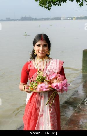 Ritratto di una bella giovane donna indiana in un tradizionale sari, indossando gioielli e braccialetti d'oro, tenendo in mano un piatto pieno di offerte religiose Foto Stock