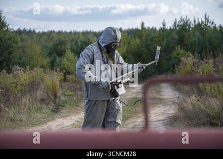 Un militare con una tuta protettiva e una maschera antigas conduce la ricognizione delle radiazioni sul campo Foto Stock