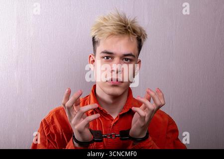 Un giovane uomo in una veste da prigione arancione con le manette sulle mani Foto Stock