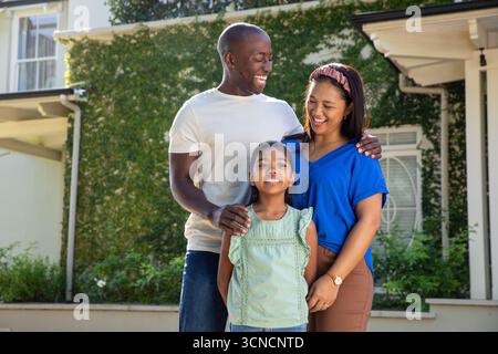 Famiglia variegata in piedi sui gradini del portico di casa suburbana che mostra edera e arbusti Foto Stock