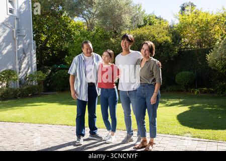 Famiglia diversificata di quattro persone in piedi insieme su un sentiero lastricato di pietra nel cortile posteriore con finestra bianca Foto Stock