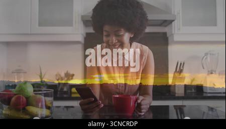 In mano tazza rossa, donna in camicia rosa che controlla lo smartphone al bancone della cucina, con cesto di frutta Foto Stock