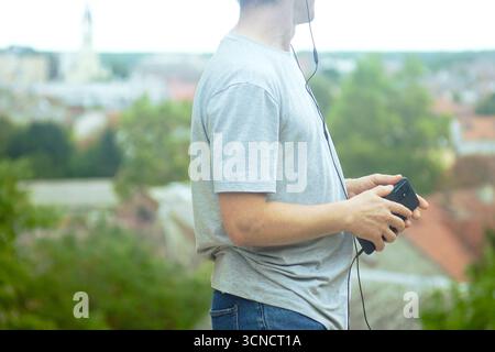 Turista che tiene in mano lo smartphone con le cuffie mentre esplora la città. Concetto di viaggio con audioguida, tour a piedi autonomo, visita turistica indipendente Foto Stock