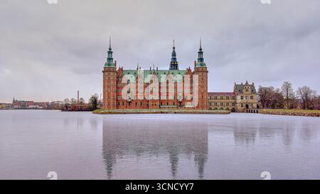Il maestoso castello di Frederiksborg si riflette su un lago ghiacciato sotto un cielo invernale grigio, che mostra la classica architettura rinascimentale nella tranquilla Hillerod, Den Foto Stock
