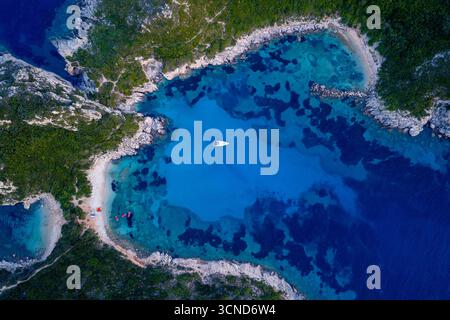 Zenith veduta aerea di uno yacht bianco solitario ormeggiato nelle acque turchesi trasparenti di una baia isolata a Porto Timoni, Corfù, circondata da un dra Foto Stock