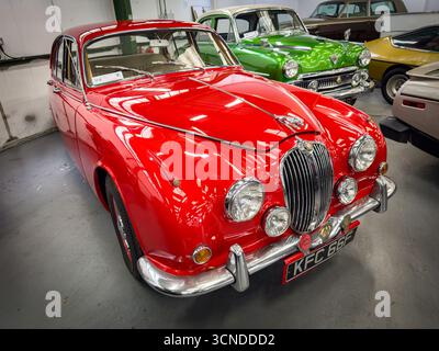 Classica auto rossa Jaguar Mark 2 in mostra in uno showroom di auto d'epoca con diverse auto storiche sullo sfondo Foto Stock