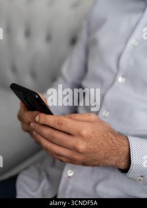 Uomo in camicia da lavoro che tiene lo smartphone, controlla i messaggi. Concetto di comunicazione, business e tecnologia moderna. Foto Stock