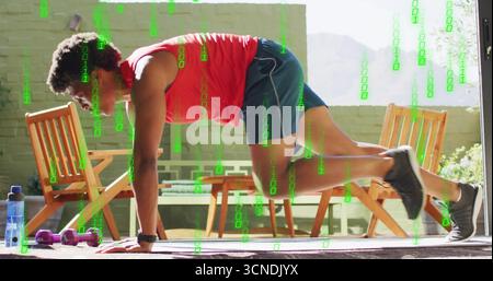 Uomo in abbigliamento sportivo che fa alpinismo sul patio con tappetino per yoga, manubri, bottiglia e tracker Foto Stock