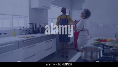 Tritare verdure da una coppia anziana che indossa grembiuli in cucina, con macchina per il caffè e bicchieri da vino Foto Stock