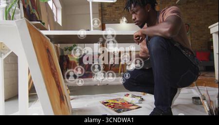 Tela dell'artista accovacciata sul pavimento dello studio, con pennello, materiali d'arte e icone utente sovrapposte Foto Stock