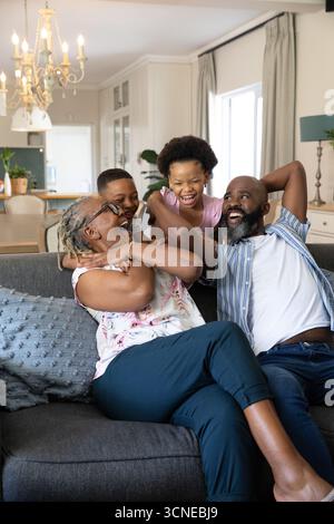 Famiglia afroamericana che ride e si rilassa insieme sul divano grigio in un luminoso soggiorno Foto Stock