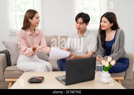 L'agente immobiliare asiatico professionale discute l'accordo di acquisto di abitazioni con clienti adulti nel loro accogliente salotto guida alla pianificazione finanziaria Foto Stock