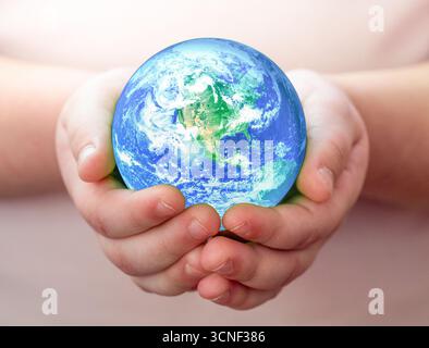 Un bambino tiene un globo nelle sue mani. Il globo è blu e verde ed è circondato da uno sfondo bianco. Concetto di meraviglia e curiosità su t Foto Stock