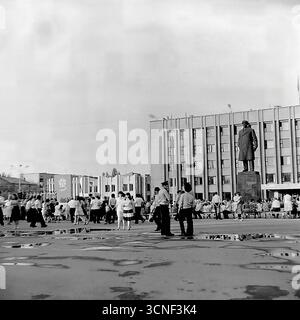 I residenti e le famiglie con bambini passeggiano attraverso la piazza centrale della Rivoluzione d'ottobre (ora piazza Soborna) vicino al monumento Lenin durante la celebrazione della giornata della città a Sloviansk, URSS, il 6 settembre 1985. Questa autentica fotografia di reportage in bianco e nero cattura l'atmosfera vivace di un festival pubblico e di un raduno di massa, con persone che si godono la vacanza insieme nonostante le pozzanghere di una pioggia precedente, mostrando una tipica scena della vita civica dell'epoca sovietica Foto Stock
