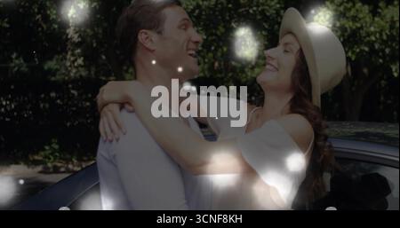 Abbracciare la coppia ridendo nel vialetto sotto la luce del sole, indossare un vestito, un cappello di paglia accanto all'auto parcheggiata Foto Stock