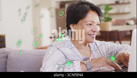 Donna indiana anziana seduta sul divano nel soggiorno, con laptop, icone ecologiche, spazio per copiare Foto Stock