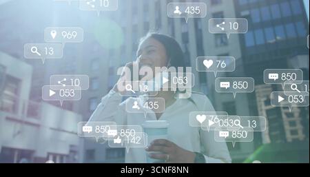 Donna asiatica sorridente in viaggio d'affari che tiene in mano smartphone e caffè sulla strada della città con icone sociali Foto Stock