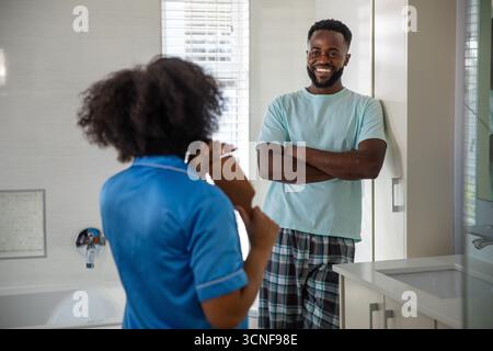 Diverse coppie in piedi nel bagno di casa spazzolando i capelli ricci con la spazzola, sorridendo Foto Stock