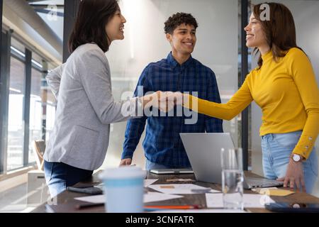 Diversi colleghi stringono la mano sul tavolo da conferenza in ufficio intorno al computer portatile e al caffè Foto Stock