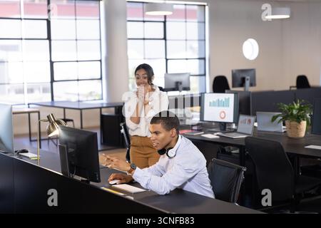 Colleghi afroamericani che collaborano alle carte utilizzando monitor e laptop in ufficio Foto Stock