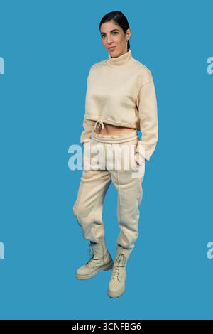 Donna in piedi a tutta altezza che indossa una tuta moderna in due pezzi e stivali su sfondo blu Foto Stock