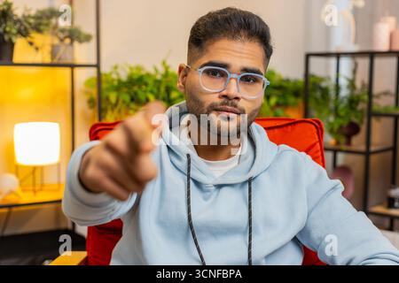 Ciao a te. Stretto infelice indiano che punta il dito della mano verso la macchina fotografica, sembra arrabbiato, fa scelta, sceglie colpevole, nota sospetta, accusa per errore nella stanza di casa. Arabian Guy siede sulla sedia Foto Stock