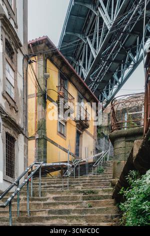 Scala di pietra urbana che conduce al Ponte d'acciaio a Porto, Portogallo. Vicolo storico, edificio giallo, gradini pedonali, contrasto architettonico, viaggio Foto Stock
